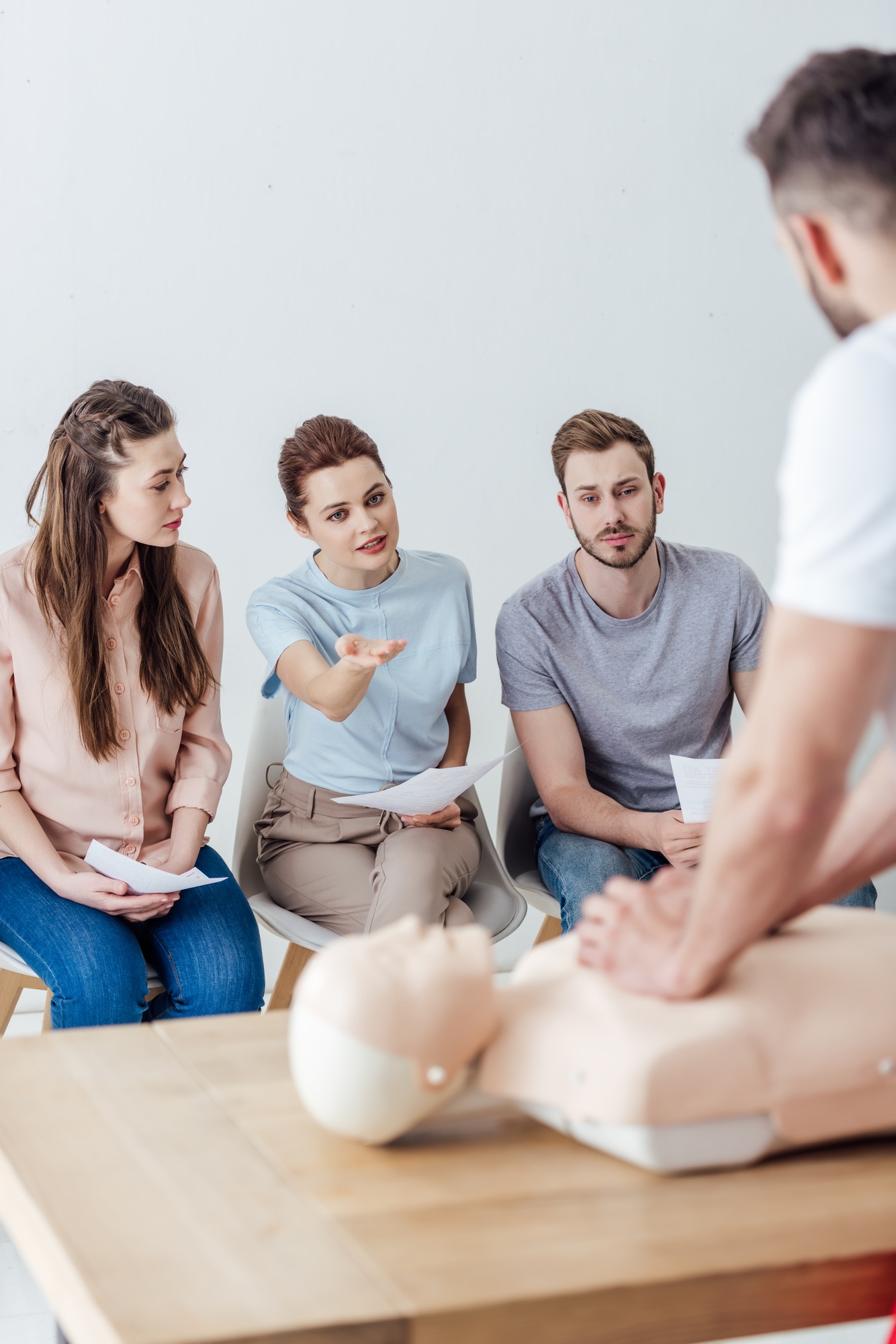 instructor performing chest compression on dummy during cpr training class with group of people